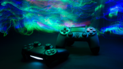 Two black PlayStation controllers lit up by blue and green techno lights against a black bakground