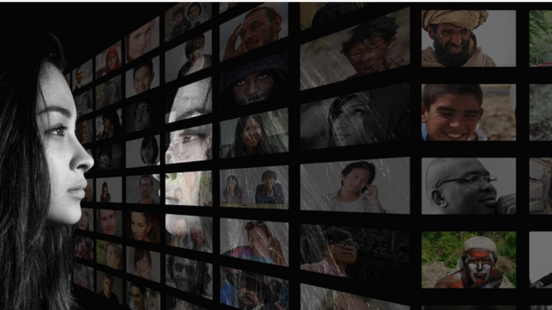 Photo of a person in black and white with long hair looking at different people through a variety screens in front of them.