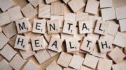 A series of wooden Bananagram letters spelling "MENTAL HEALTH" on a background of blank tiles.